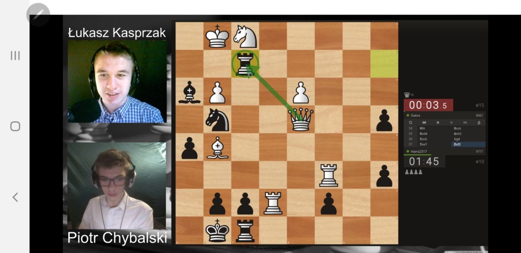 Zdjęcie ze streamingu turnieju, na którym widać dwóch sędziów,  komentujących rozegraną partię szachów, widoczną po prawej stronie ekranu.