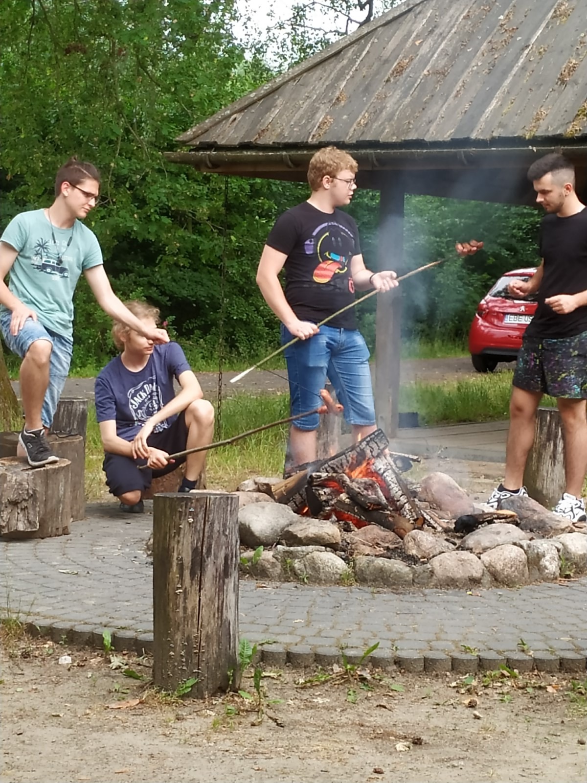 Wychowankowie pieką kiełbaski na ognisku.