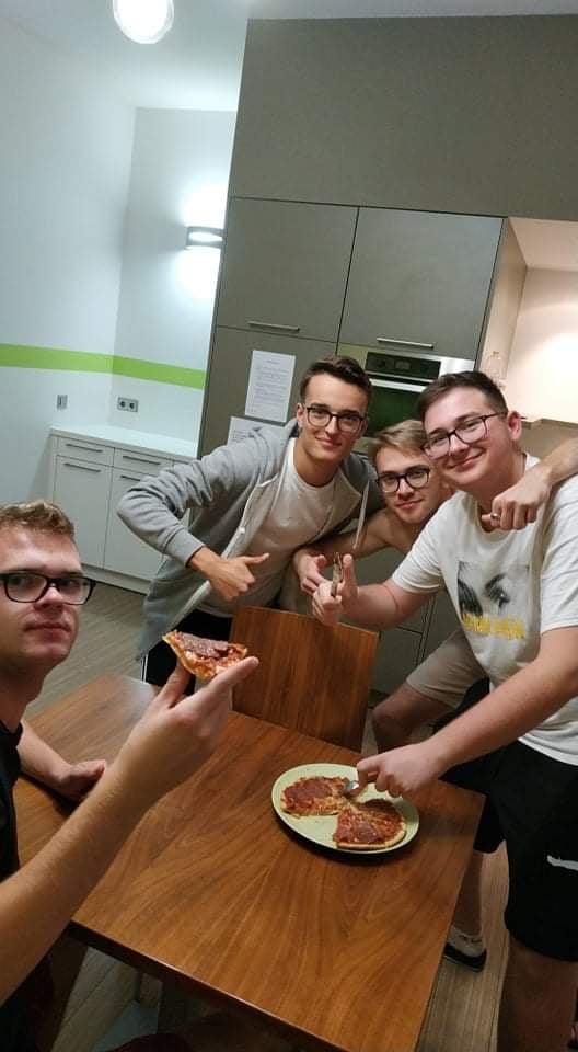 Uczniowie w kuchni jedzą pizzę.