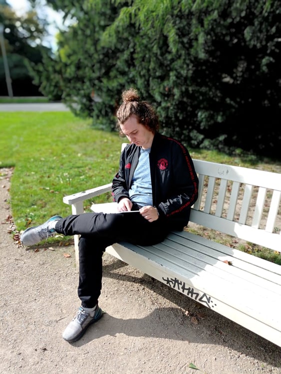 Uczeń czyta ksiżkę na ławce w parku.