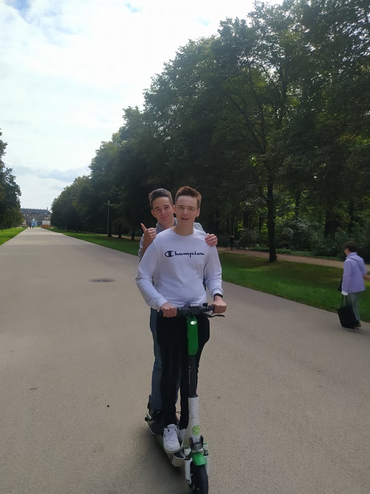 Dwóch uczniów na hulajnodze w parku.