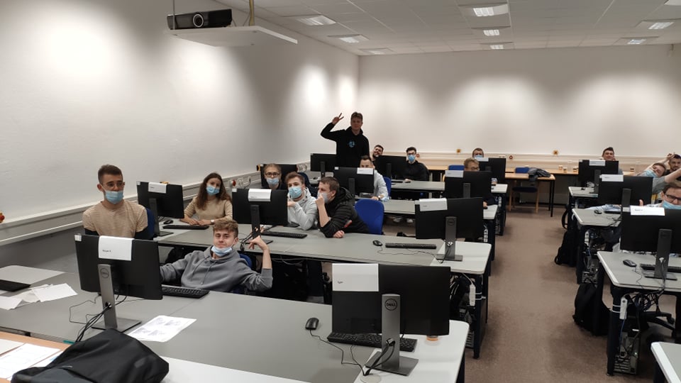 Uczniowie w sali szkoleniowej siedzą przy komputerach.