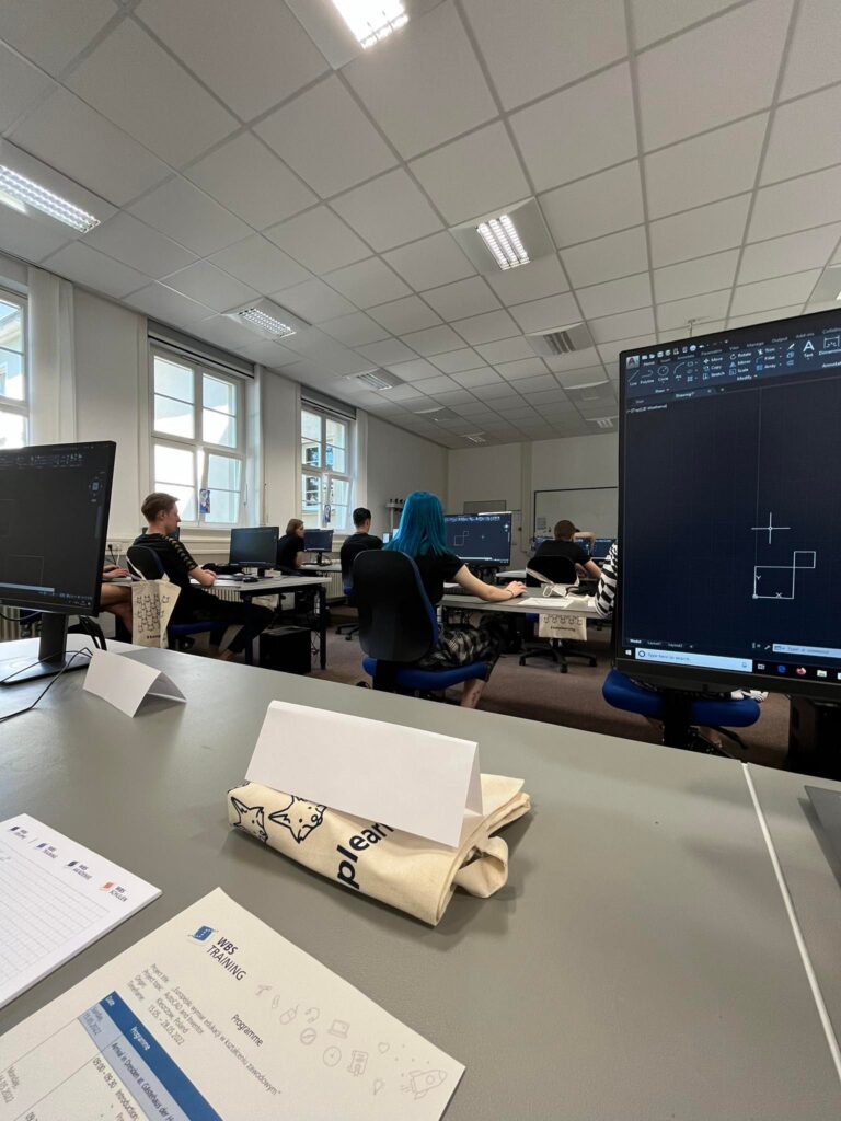 Uczniowie siedzą przy komputerach.