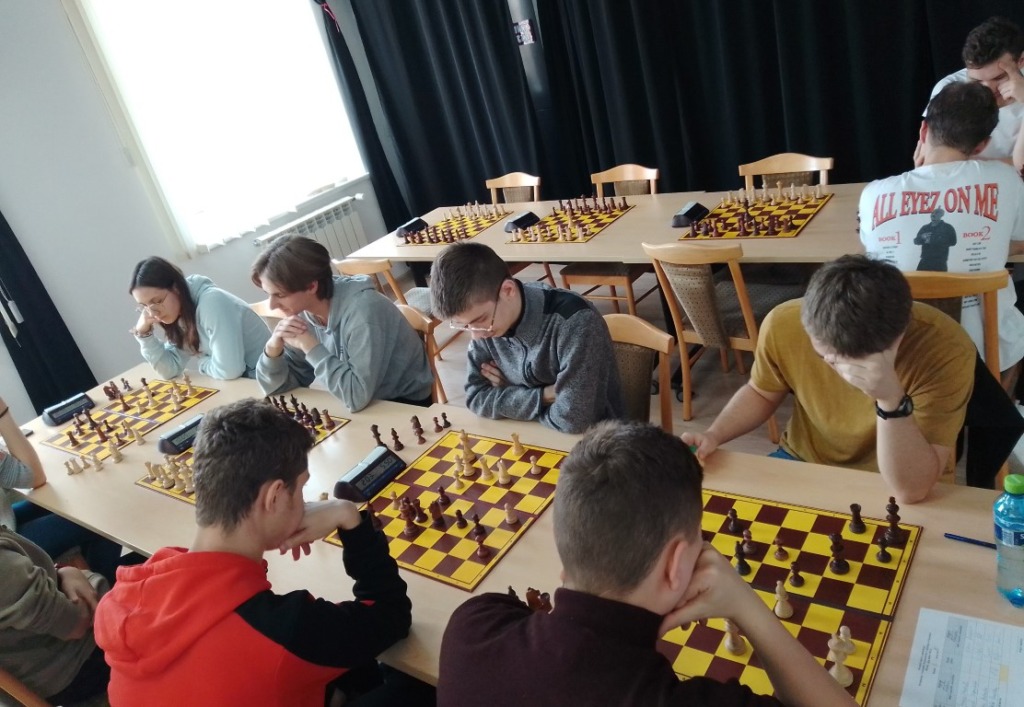 uczniowie siedzą przy szachownicy