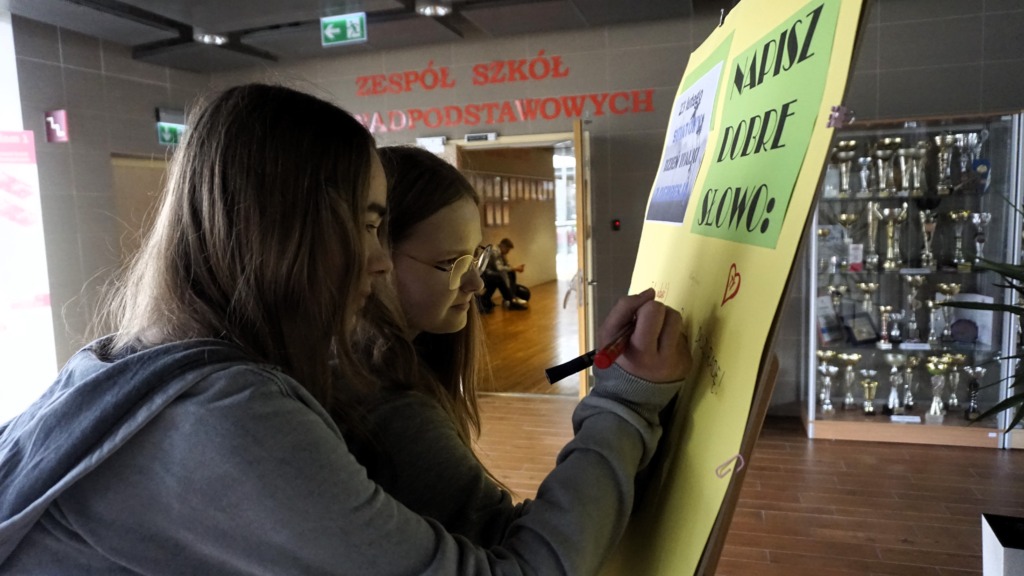7.	Dwie uczennice piszą dobre słowa na żółtej antydepresyjnej tablicy.